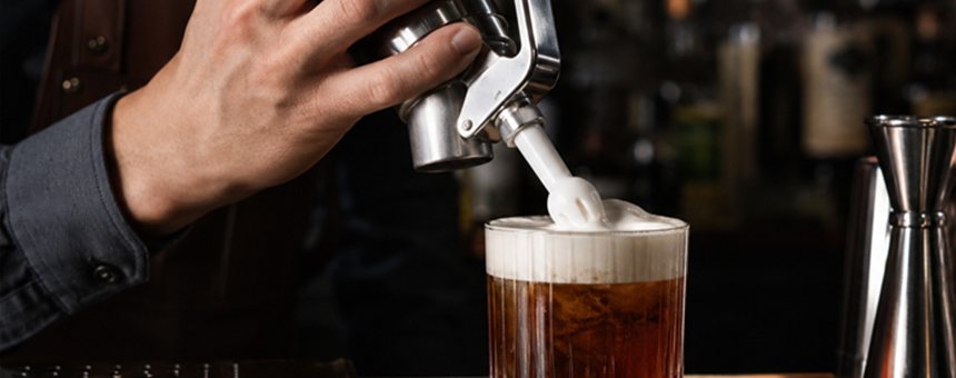 Cream whipper charged with N₂O dispensing foam into a glass on a bar bench